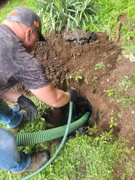Septic technician working at an excavated tank access point during residential service in Clark County.